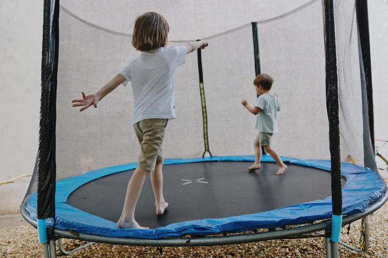 Two children joyfully bouncing on a trampoline, showcasing excitement and energy. The bright colors and playful atmosphere create a fun vibe for outdoor activities.