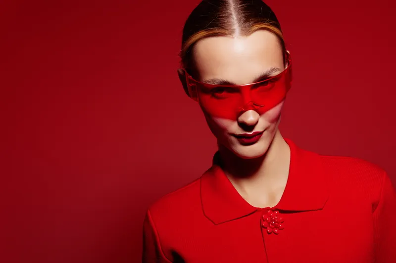 Woman with slicked hair wearing red sunglasses and red outfit poses confidently against red background. Concept of fashion, style, bold colors, and modern portrait photography.