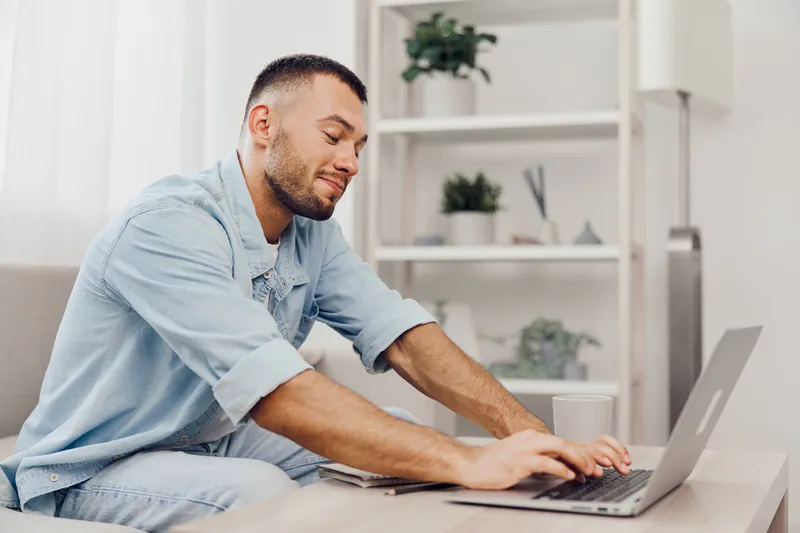A focused man working on a laptop, embracing soft masculinity amidst a blend of personal and professional life, while showcasing authentic imperfection.