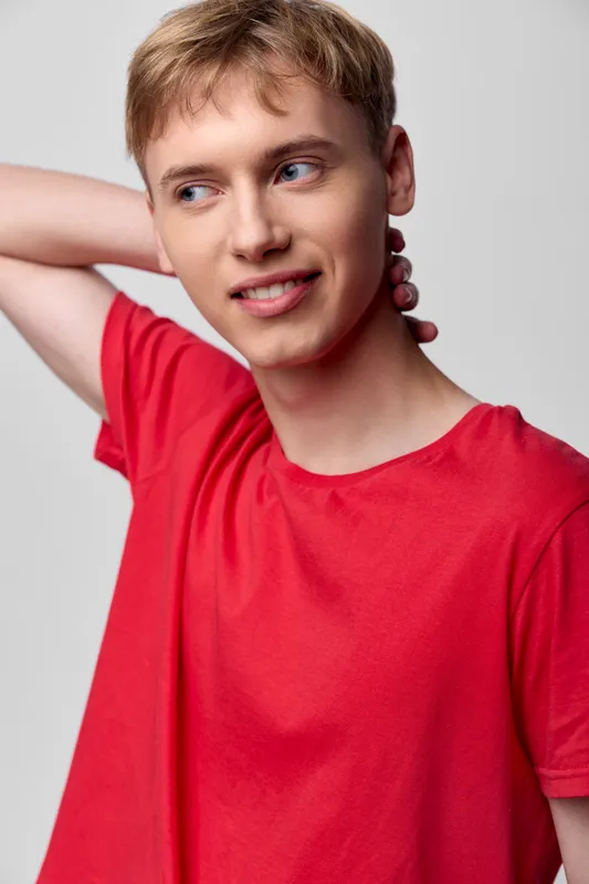 Casual portrait of a young man wearing a red shirt, with a hand at the neck and a sideways gaze, studio lighting, clean background, conveying relaxed fashion and everyday style