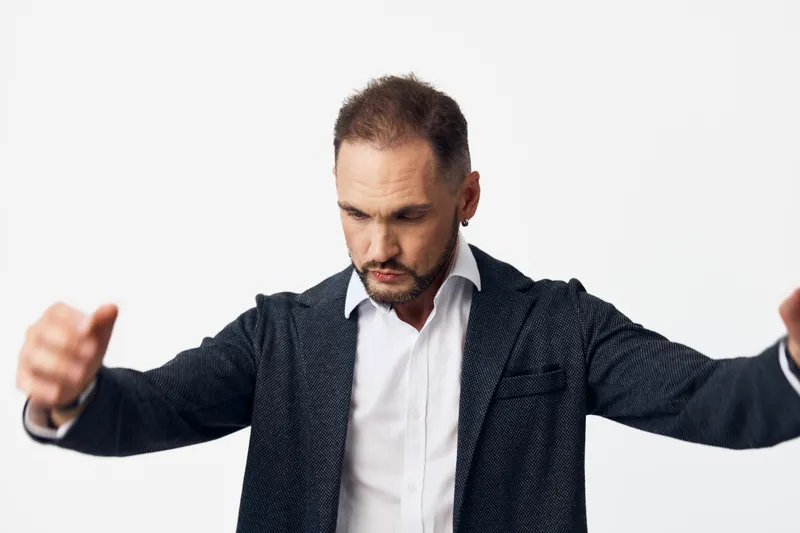 A business professional man stands with arms outstretched against an isolated colored background, conveying confident leadership, focused emotion, and strong determination in a studio portrait.