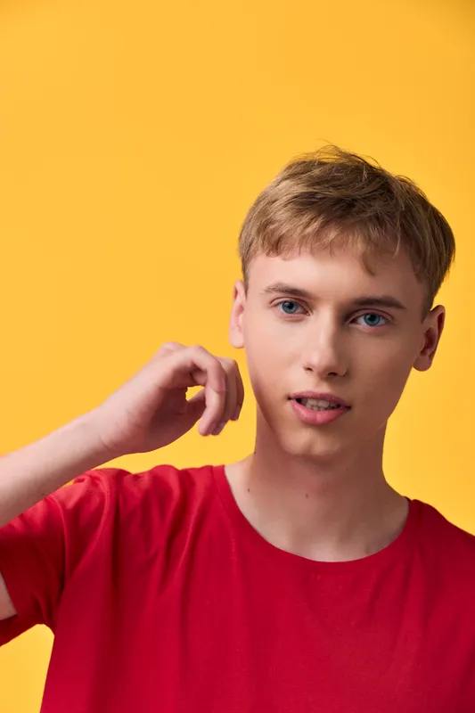 Young man wearing a red shirt in a studio with a yellow background, casual pose, relaxed expression, fashion vibe for lifestyle and marketing use