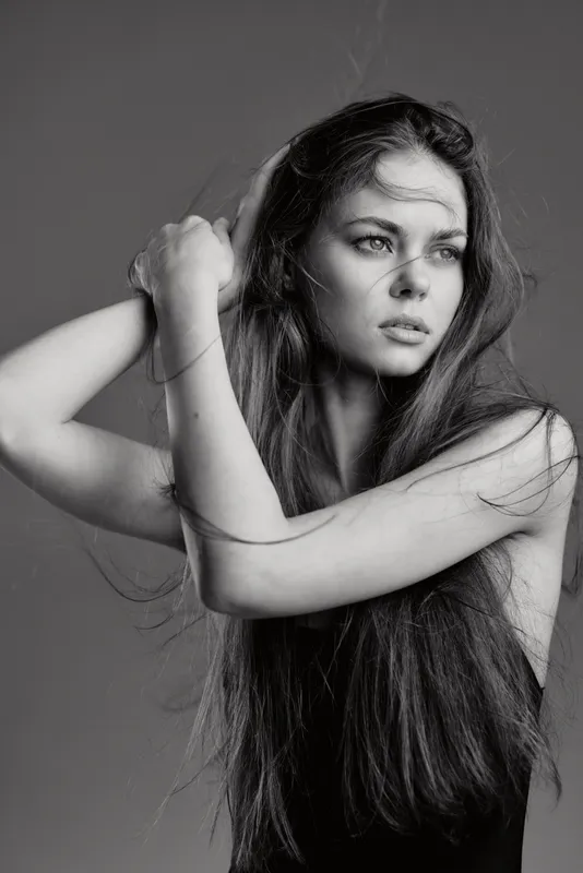 Black and white portrait of a thoughtful woman with long hair and expressive eyes in studio lighting.