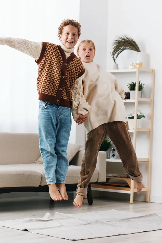 Authentic candid scene of playful siblings jumping together at home, capturing school age energy and a cozy lifestyle moment filled with warmth, joy, and everyday friendship.