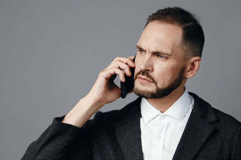 A professional businessman on a call against an isolated colored background, expressing focused emotion, confidence, and contemplation in a modern corporate setting suitable for branding.
