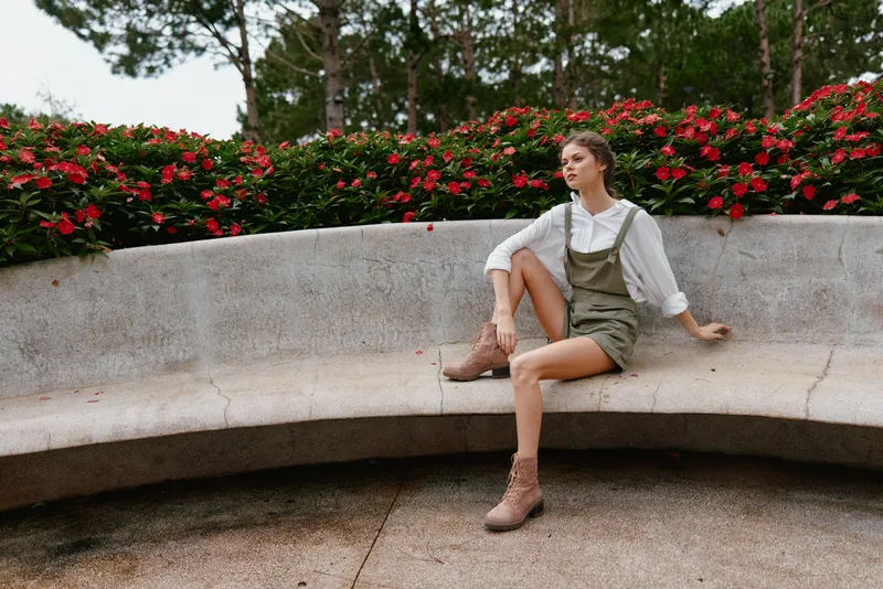 Young woman in casual attire sitting on a bench surrounded by vibrant flowers, showcasing a serene expression in a natural outdoor setting