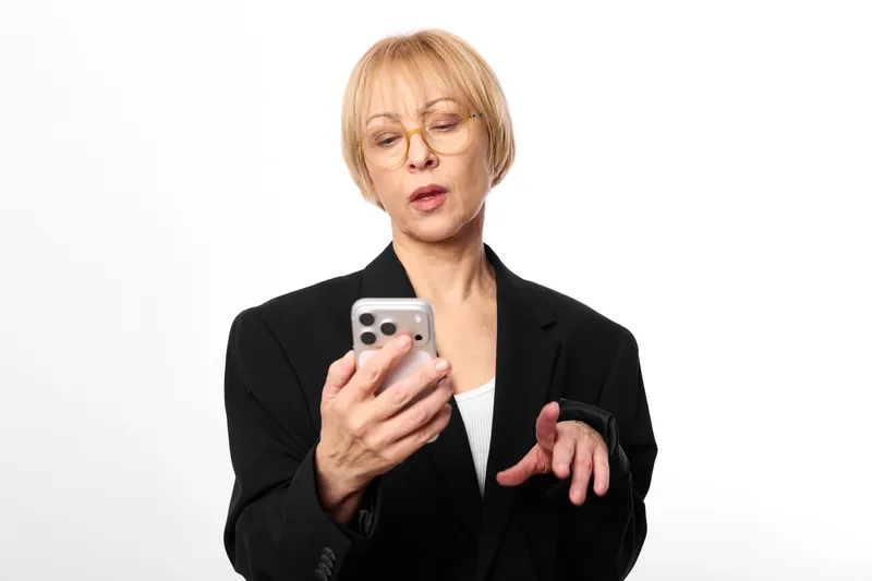 Woman with smartphone, stress and anxiety, burnout concept, overwhelmed expression, mature blazer portrait on white background, eyes closed holding phone, hand gesture shows pressure, mental health