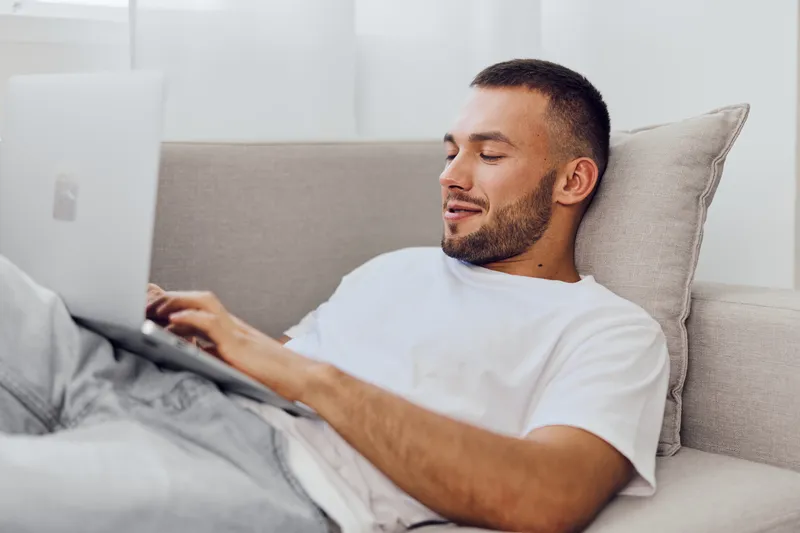 Relaxed man enjoying a digital detox on his laptop, embracing solitude while balancing personal and work life. A moment of authentic imperfection captured in home comfort.
