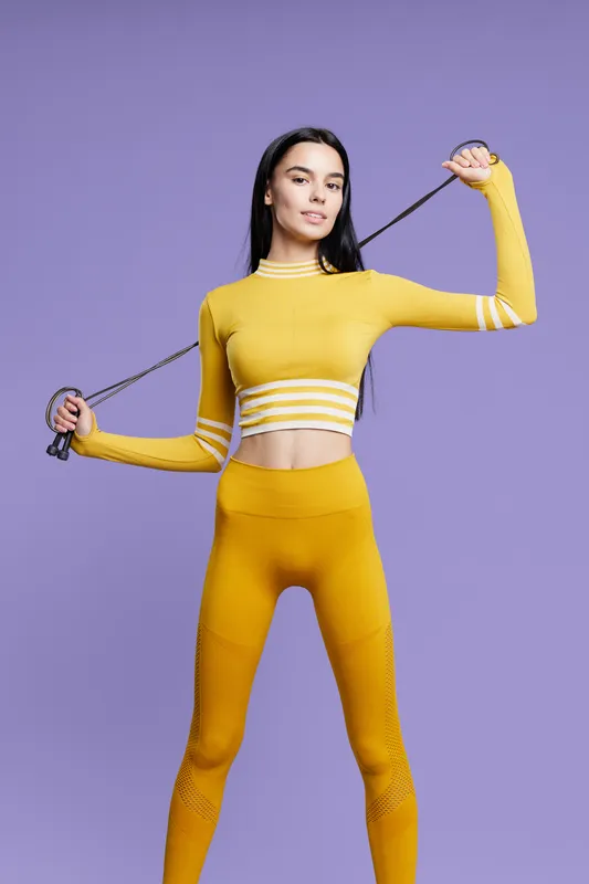 Woman sport fitness stretching with resistance band, wearing yellow activewear, isolated on purple background, slim healthy young female performing exercise confidently.