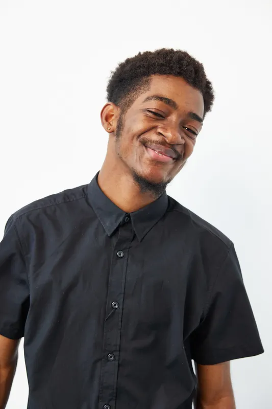 Smiling African American man wearing a black shirt, showcasing joy and confidence against a minimalistic background. Perfect for lifestyle and portrait themes.