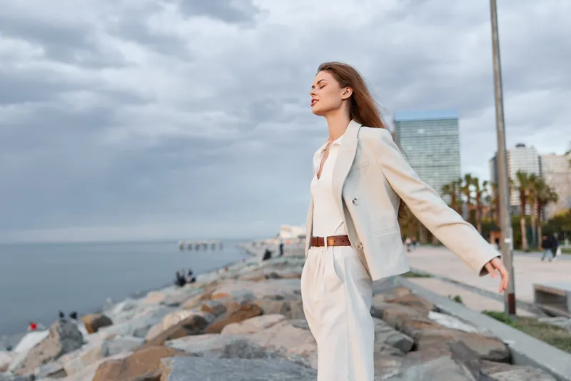 Confident woman in a stylish business suit by the seaside, showcasing elegance and determination against a cloudy sky backdrop.