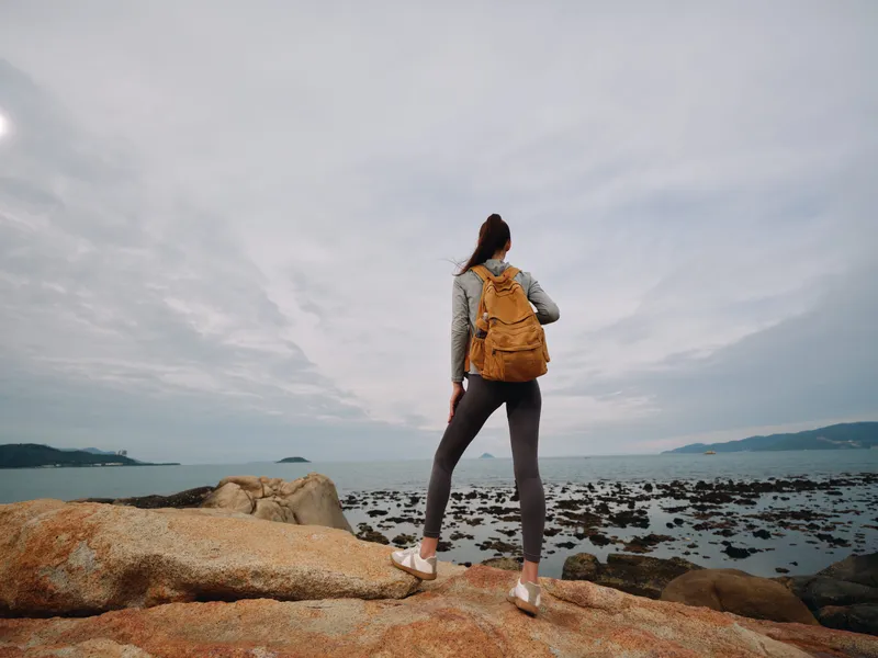 Young woman enjoying a scenic coastal view, wearing sporty activewear and a backpack, capturing the essence of adventure in nature