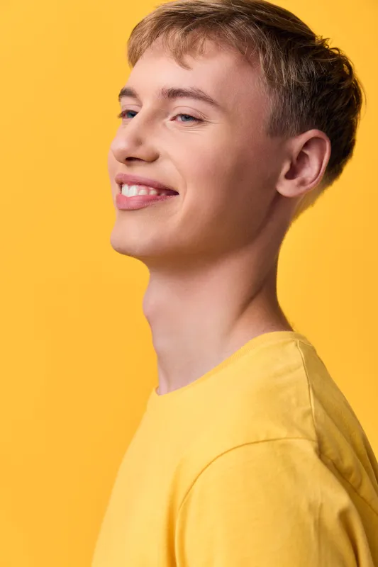 Smiling man in a yellow shirt against a bright yellow backdrop, showcasing warm casual fashion, upbeat mood, clean lifestyle vibe, confident pose and modern studio lighting
