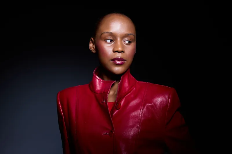 Portrait of a confident dark skinned African woman wearing a red leather jacket, looking sideways against a dark background. Concept of fashion, elegance, and empowerment.