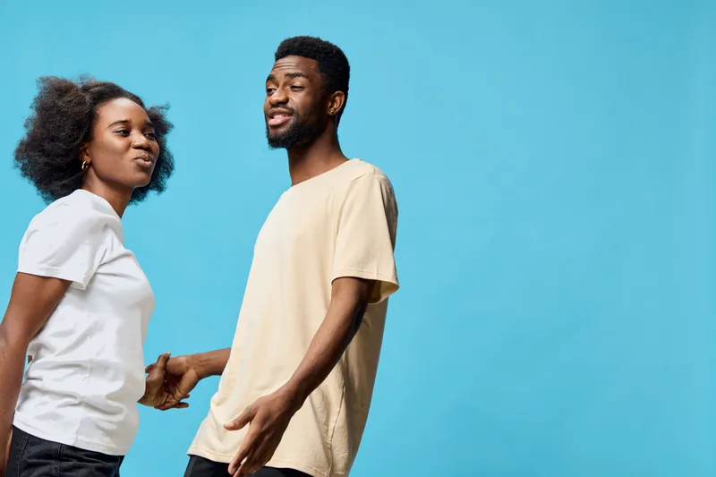 Young diverse couple enjoying a playful moment together against a vibrant blue background, showcasing their casual outfits and joyful expressions