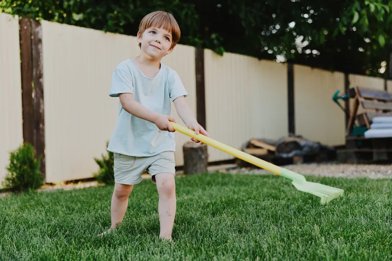 Happy boy playing outside with a yellow shovel, enjoying a sunny day in the garden while exploring nature and fostering creativity in a playful environment.