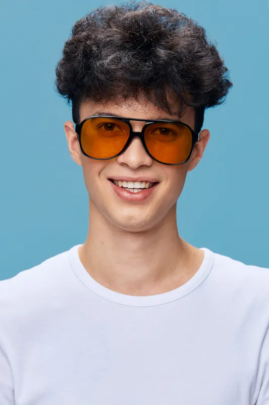 smiling man wearing large orange sunglasses and white t-shirt with curly hair on blue background, casual style with happy facial expression and youthful vibe