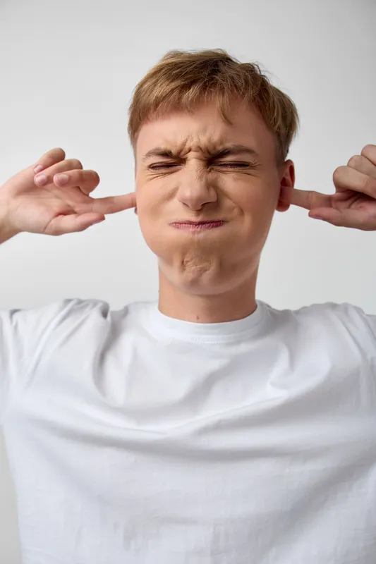 Man restrains sound by plugging ears, ear protection, noise discomfort, hearing strain, seeking silence, sound barrier in a loud indoor setting, casual attire, candid moment of relief from noise