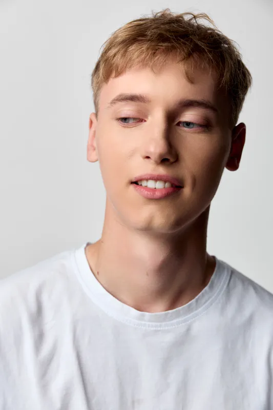 Young man in a white tee gazes aside with a subtle smile, showcasing casual style, everyday comfort, and relaxed mood suitable for lifestyle and fashion scenes