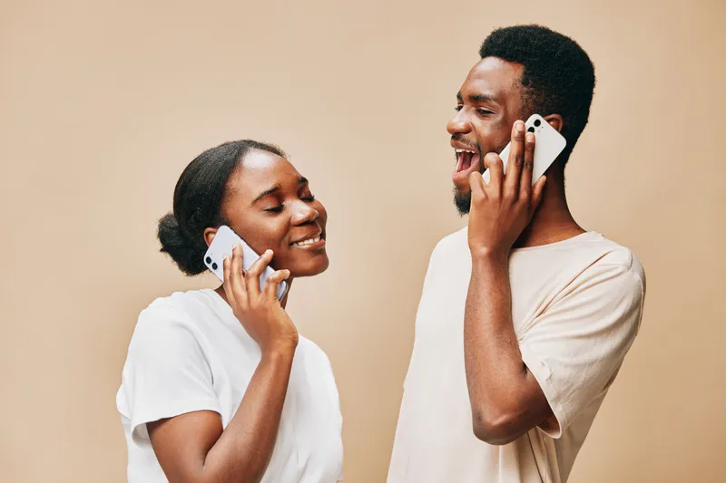 Happy couple talking on smartphones, sharing joyful moments, natural expressions, neutral background, modern lifestyle, communication, connection, engagement