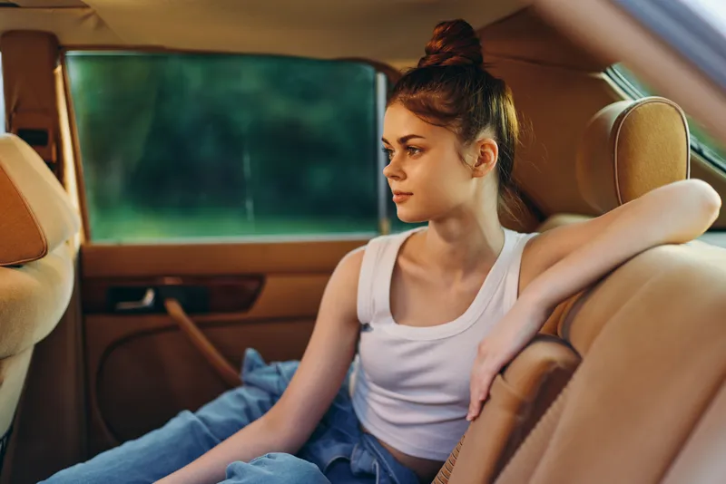 Young woman relaxing in car with casual outfit and natural expression, featuring a vibrant green background. Perfect for lifestyle and travel themes.