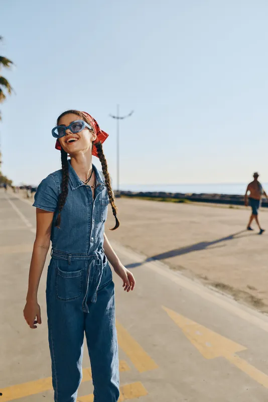 lifestyle woman in modern boho-western denim street style smiling outdoors with sunglasses and red bandana, bright film color, casual summer vibe, carefree and happy
