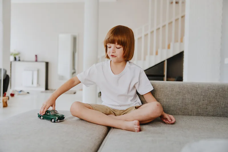 Happy boy playing with a toy car in a modern living room, surrounded by soft light and minimalistic decor. Perfect for capturing joy and childhood moments.