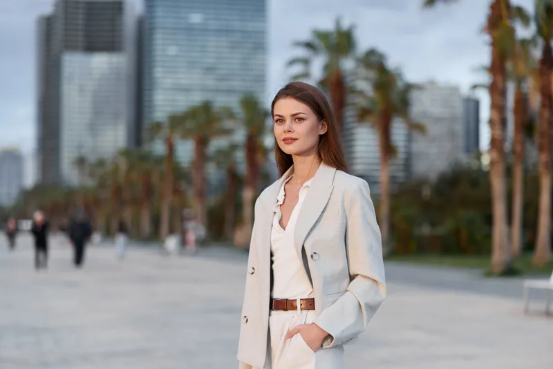 Confident woman in business attire stands in urban setting, showcasing professionalism and elegance against modern city backdrop.