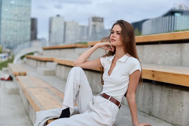 Business woman in elegant attire, sitting on bleachers, showing confidence and style against an urban backdrop, perfect for professional themes.