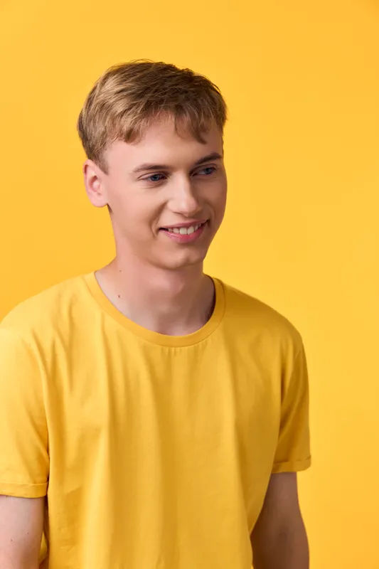 Man, smiling, wearing a yellow shirt in a studio setting with a warm background, casual fashion shot highlighting mood, confidence, and simplicity