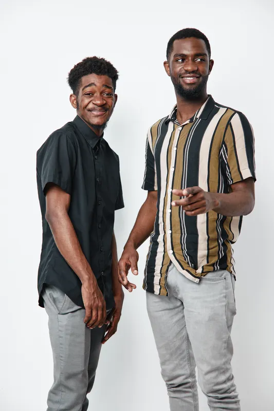 Two young black men standing together smiling and posing on white background casual clothing with striped shirt and black shirt for friendship and happiness.
