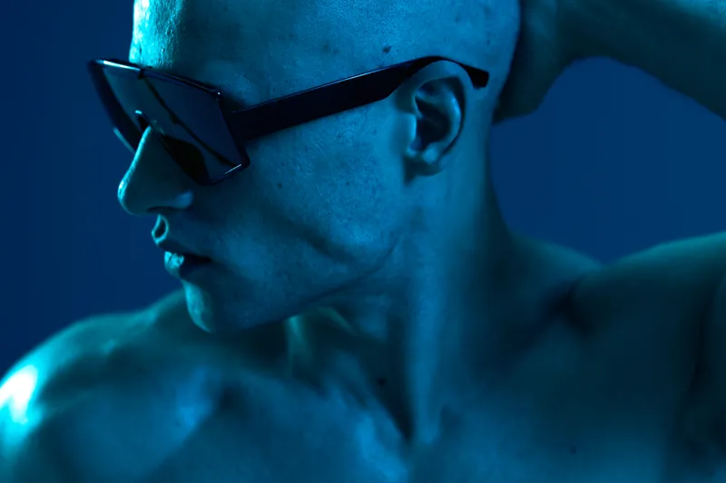 Stylish man in sunglasses with a vibrant blue background, showcasing a modern aesthetic and a confident expression. Perfect for fashion and lifestyle themes.