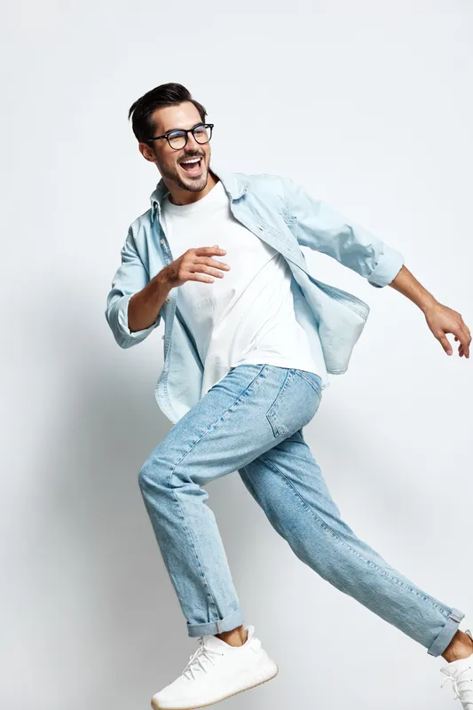 Full body smiling happy cheerful young man wearing casual outfit, running joyfully with glasses, isolated on plain light background. People lifestyle concept