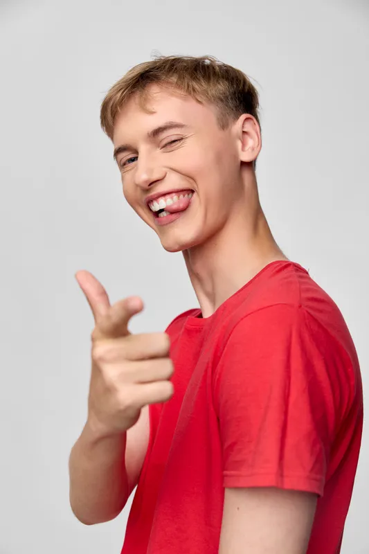 Smiling man, red shirt, pointing gesture, friendly pose for promotional or lifestyle use in ads, conveying confidence, approachability and positive energy suitable for marketing and social media