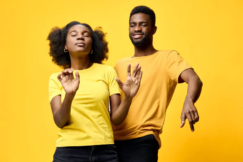 Young African American couple dancing joyfully in vibrant yellow T shirts against a bright yellow background, conveying happiness and carefree emotions, perfect for lifestyle themes