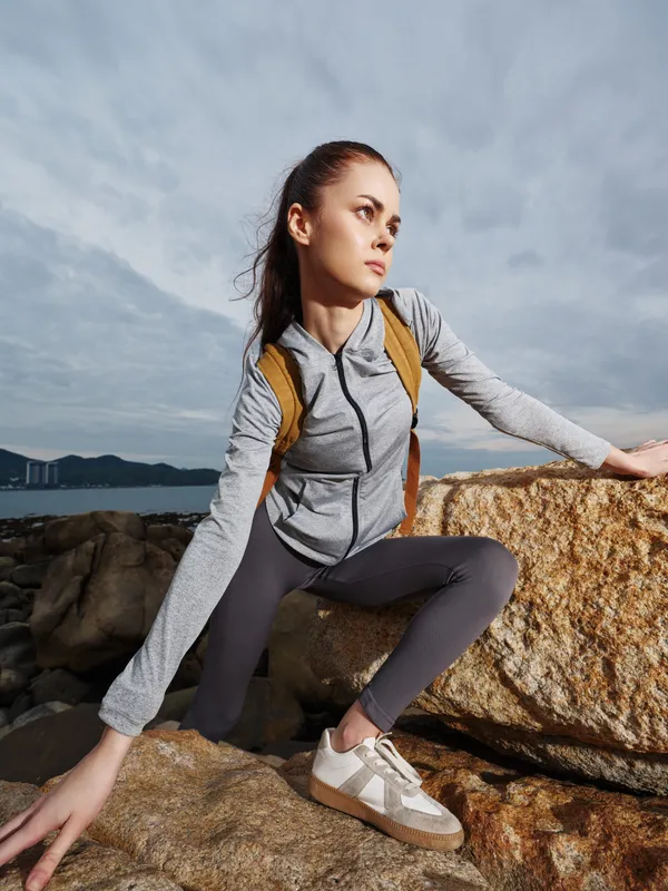 Young woman in sporty attire climbing a rock, showcasing determination and strength against a cloudy backdrop, ideal for fitness and outdoor themes