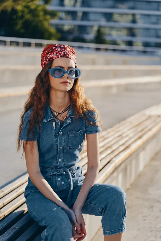 Lifestyle woman in modern boho-western denim street style wearing sunglasses and a red bandana with film color effect in outdoor urban setting.