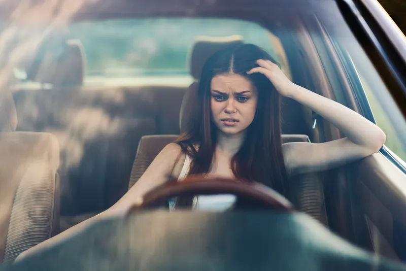 Concerned young woman expressing frustration while sitting in her car, highlighting emotions of stress and anxiety, perfect for themes of mental health and driving challenges.