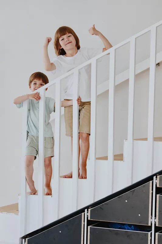 Joyful children playing on the stairs, sharing happiness and energy with carefree laughter in a bright, airy home setting, capturing the essence of childhood fun.