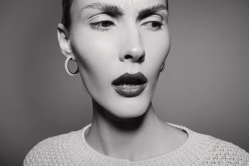 Close-up of a young Caucasian woman with pale skin showing a confused expression, wearing hoop earrings and a knitted top. Concept for doubt and uncertainty.