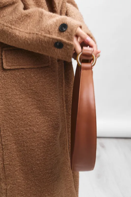 asian woman wearing a warm brown coat holds a leather handbag, presenting a chic street style moment with calm confidence and timeless fashion.