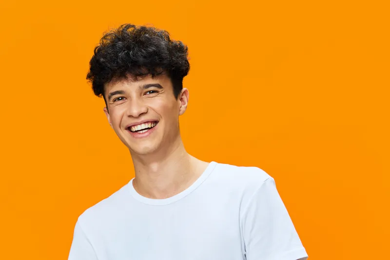 smiling man with curly hair wearing a white t-shirt on bright orange background, cheerful young adult with natural expression in casual style