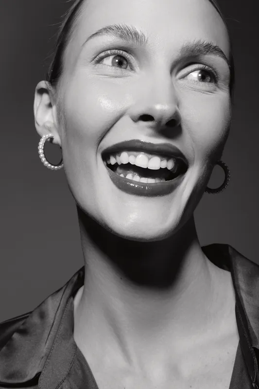 Closeup of happy young white woman with light skin smiling and wearing hoop earrings in black and white photo.