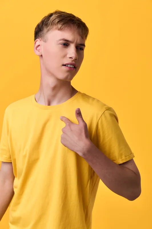 Young male in a yellow tshirt against a bright yellow background pointing at himself casual lifestyle shot with bold color and confident expression studio lighting minimal setup