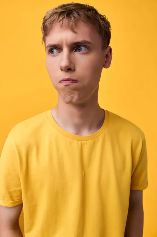 Puzzled expression on a young man wearing a bright yellow shirt against a matching yellow studio backdrop, conveying confusion, curiosity and contemplation in a clean image suitable for ads and