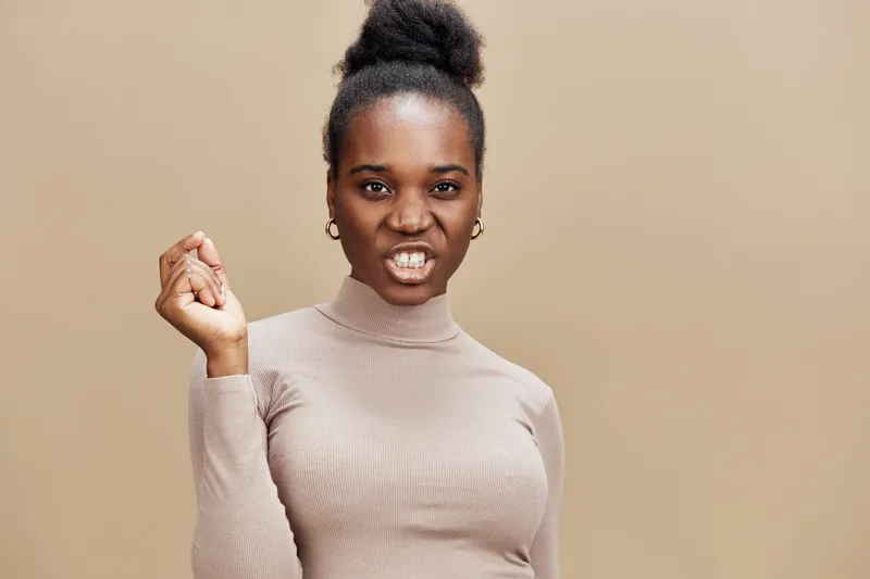 Confident Black woman in a beige turtleneck sweater, showing determination and empowerment against a soft brown background, ideal for themes of self confidence and strength