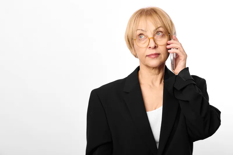 Woman senior glasses phone business communication call portrait professional corporate blazer suit, mature female holding phone to ear, calm studio portrait on white background