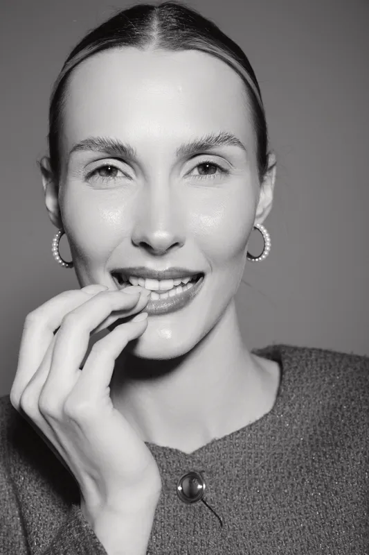 Close-up portrait of a smiling Caucasian woman with fair skin and slicked-back hair wearing hoop earrings and a textured top. Concept of beauty, confidence, and fashion.