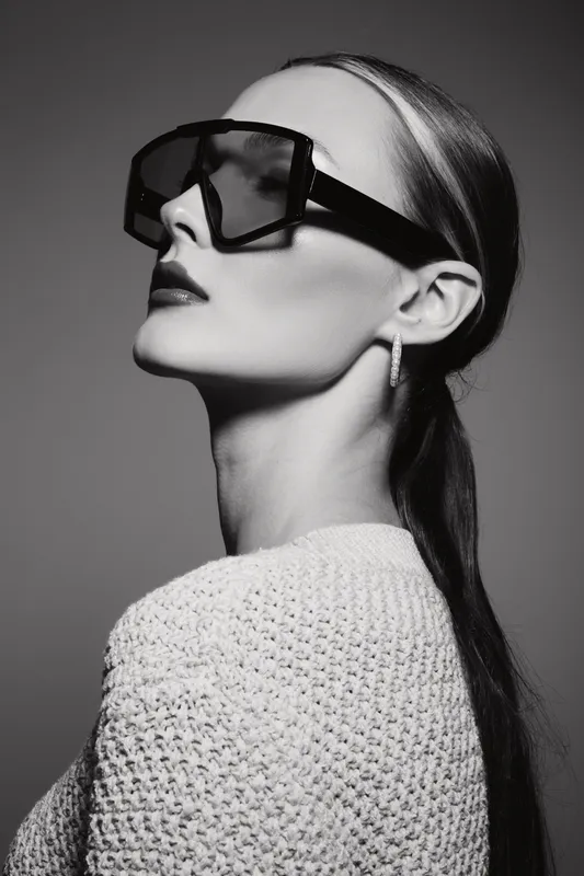 Stylish Caucasian woman with fair skin wears large black sunglasses and knitted sweater in studio portrait. Concept of fashion and elegance.