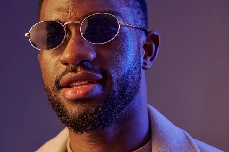 Portrait of a stylish young Black man wearing sunglasses, expressing confidence against a colorful background, ideal for fashion or lifestyle concepts